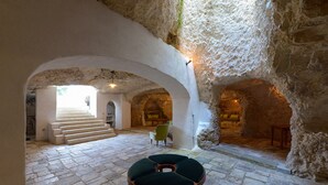 A stone interior with a circular seating area, a staircase, and a sofa in a natural cave-like setting. - Masseria Lamiola Piccola (Ostuni)