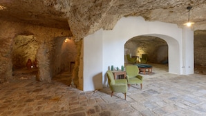 A stone-walled interior with a stone floor, green upholstered chairs, a small table, and a cactus plant. - Masseria Lamiola Piccola (Ostuni)