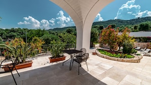 An outdoor patio with a table and chairs, surrounded by potted plants and a view of a lake and hills. - Masseria Lamiola Piccola (Ostuni)