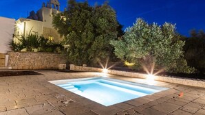 A swimming pool with a stone deck, surrounded by trees and a building with a bell tower. - Masseria Lamiola Piccola (Ostuni)