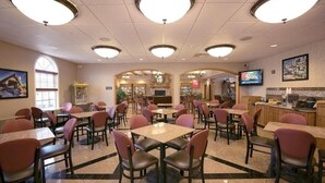 Un amplio comedor interior con varias mesas y sillas, una zona de bar y una pantalla de televisión.