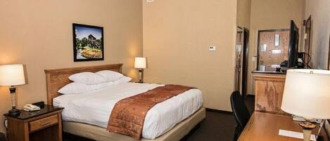 Habitación de hotel con una cama, dos mesitas de noche con lámparas, un escritorio con una silla, un televisor y un cuadro en la pared.