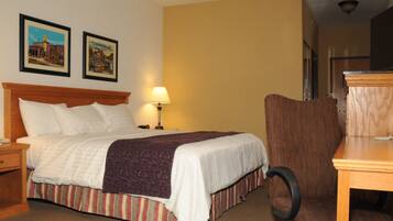 A hotel room with a bed, a desk, a chair, a lamp, and two framed pictures on the wall.