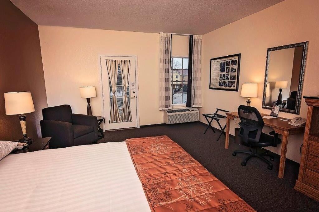 A hotel room with a bed, a desk, a chair, a lamp, a mirror, and a window with curtains.