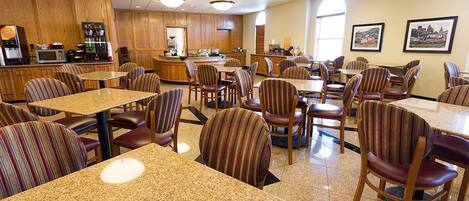 A hotel dining area with striped chairs and granite tables, a coffee station, and framed pictures on the wall.