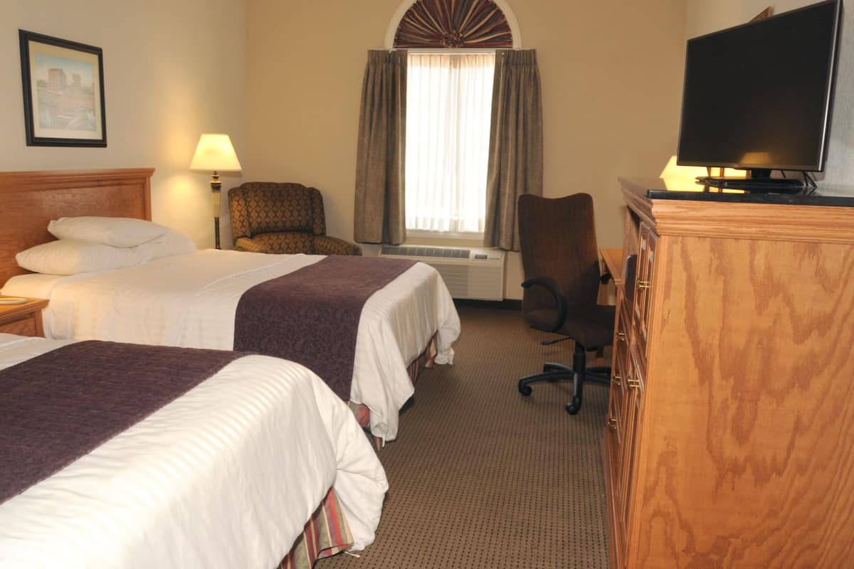 A hotel room with two beds, a desk, a chair, a television, and a window with curtains.