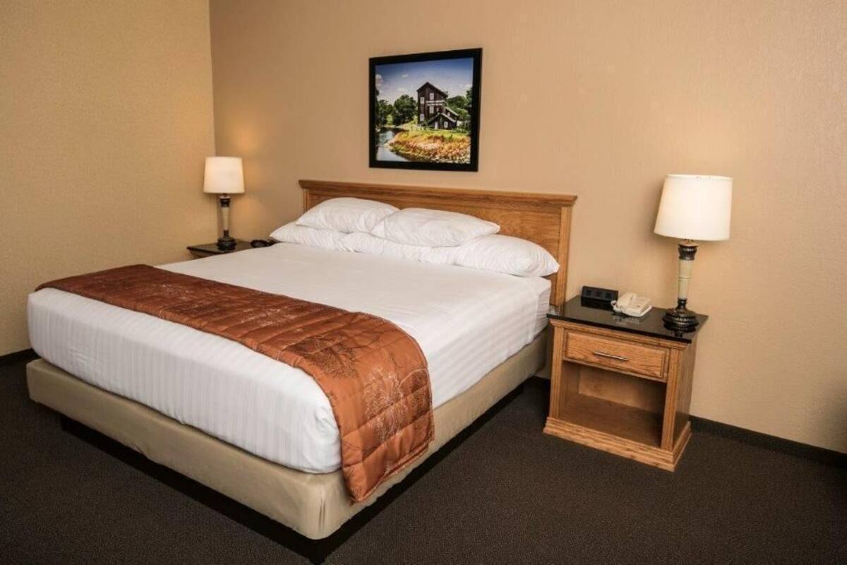 A hotel room with a bed, two bedside tables, a nightstand, a lamp, and a framed picture on the wall.
