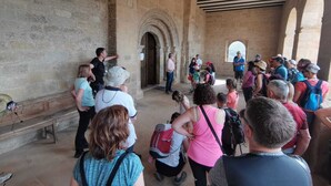 Un groupe de touristes se trouve à l’intérieur d’un bâtiment historique, dont les murs sont en pierre et le plafond en bois.