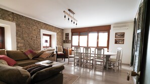 Un salon avec un mur en pierre, des meubles en bois et un coin repas comprenant une table et des chaises.