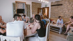 Un groupe de personnes est assis autour d’une table dans une pièce aux murs de pierre, où un téléviseur est fixé au mur.