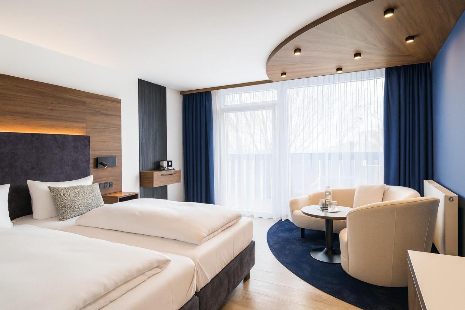Ein modernes Hotelzimmer mit einem großen Bett, einem Schreibtisch, einem Sessel und einem fenster mit Vorhängen.