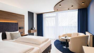 Ein modernes Hotelzimmer mit einem großen Bett, einem Schreibtisch, einem Sessel und einem fenster mit Vorhängen.