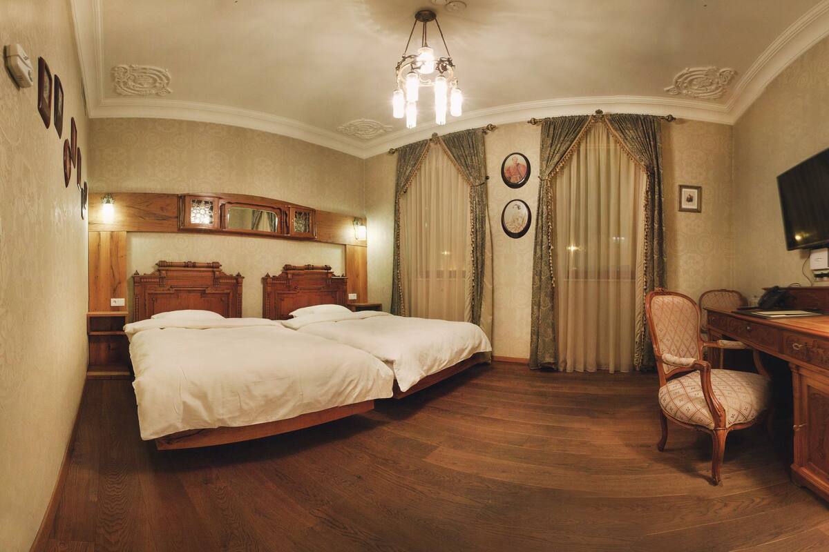 Habitación de hotel con una cama grande, un escritorio, una silla, un televisor y una araña.