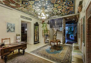 Un amplio pasillo con techo ornamentado, un candelabro, un banderín con trofeos y un escritorio de madera tradicional.