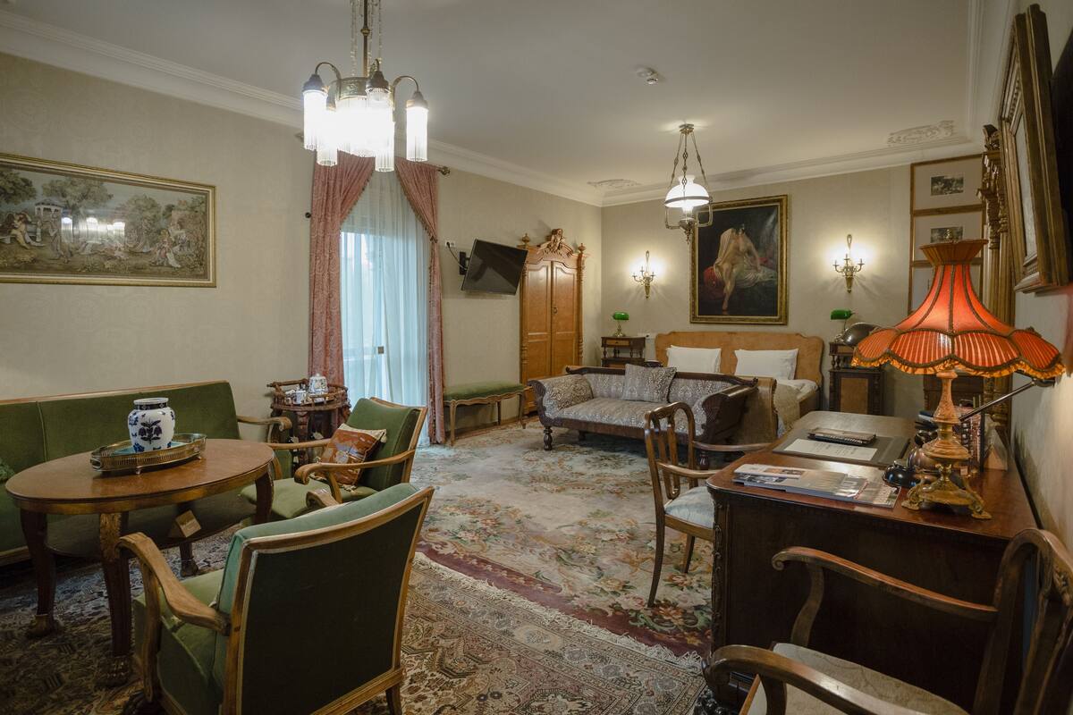 Un salón tradicional con sofá, sillones, una mesa de centro de madera, un escritorio con lámpara y un cuadro grande en la pared.
