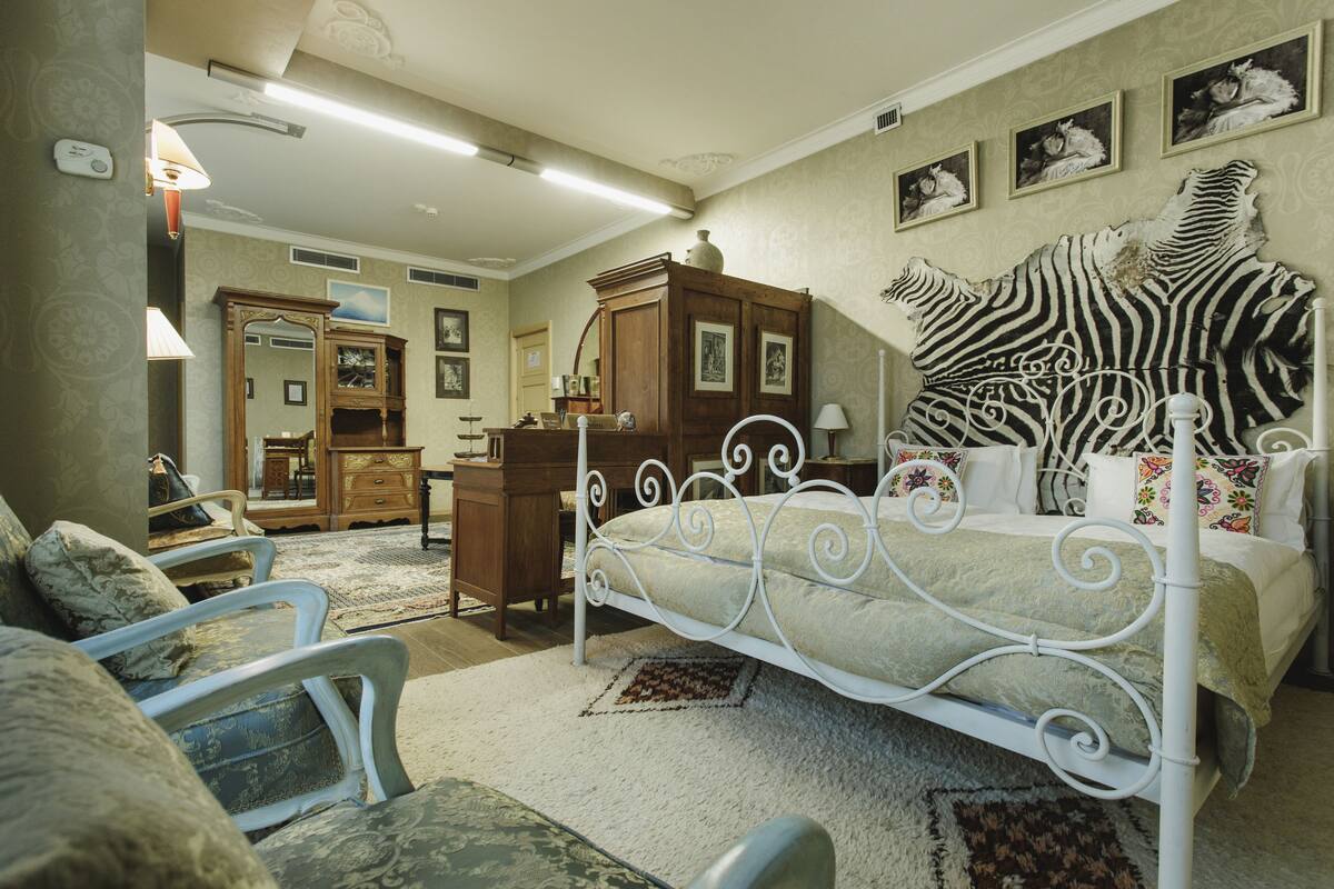 Un dormitorio con estructura de cama metálica blanca, cabecera de cebra, cómoda de madera y un espejo.