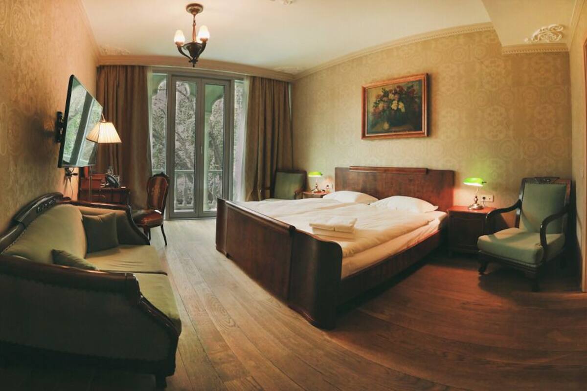 Habitación de hotel con una cama grande, un escritorio con silla, televisión y vista a árboles por la ventana.