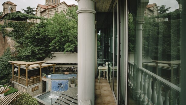 Blick auf ein Gebäude mit Poolbereich, einer überdachten Terrasse und einer Kirche im Hintergrund.