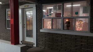 Un edificio de ladrillo con una puerta blanca identificada con la palabra “OFFICE” y una ventana que muestra un letrero que dice “VENIMOS, ESTAMOS ABIERTOS”.