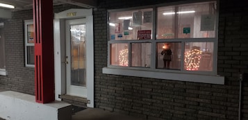 A brick building with a white door labeled "OFFICE" and a window displaying a "COME IN WE'RE OPEN" sign.