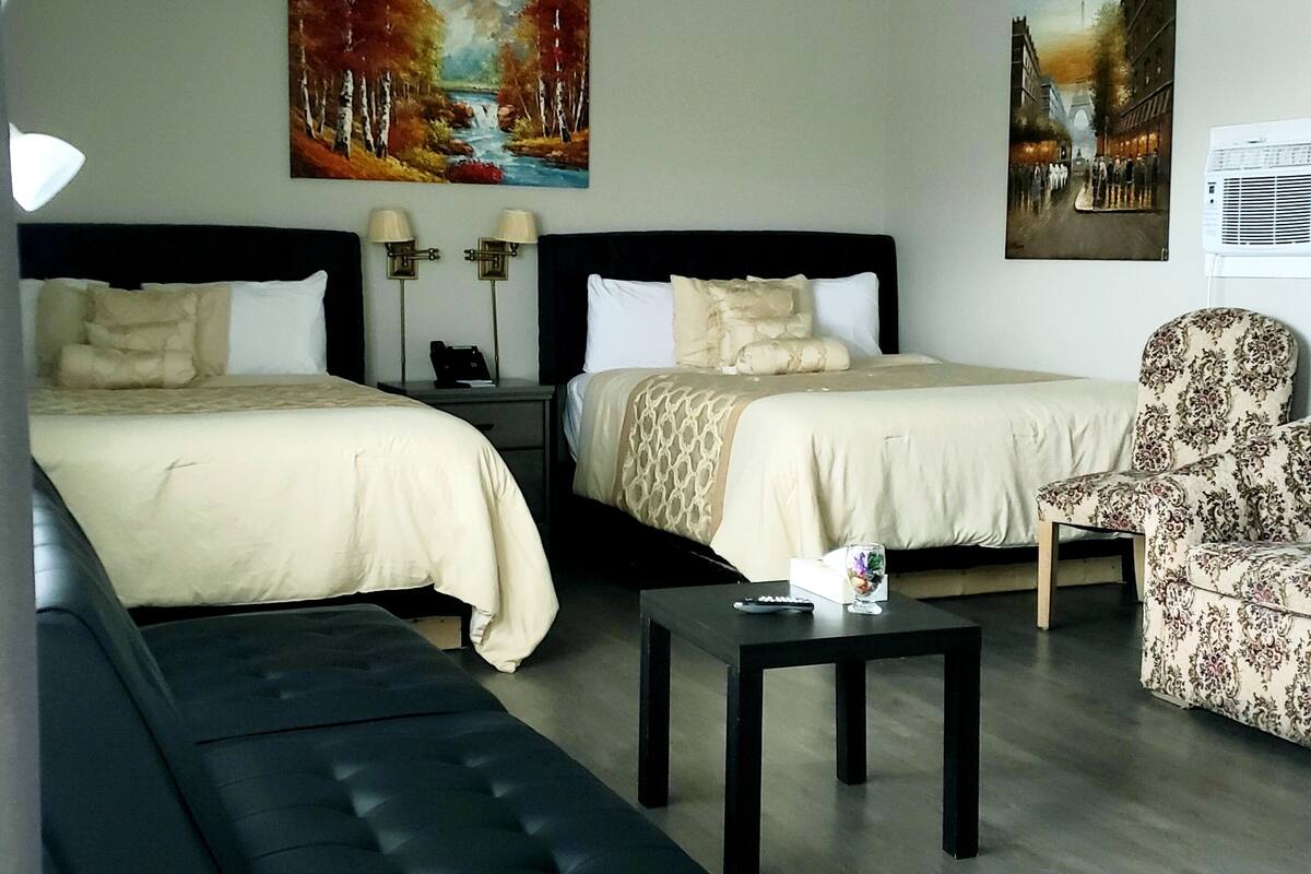 Habitación de hotel con dos camas, un sofá, una silla, una mesita y obras de arte en las paredes.