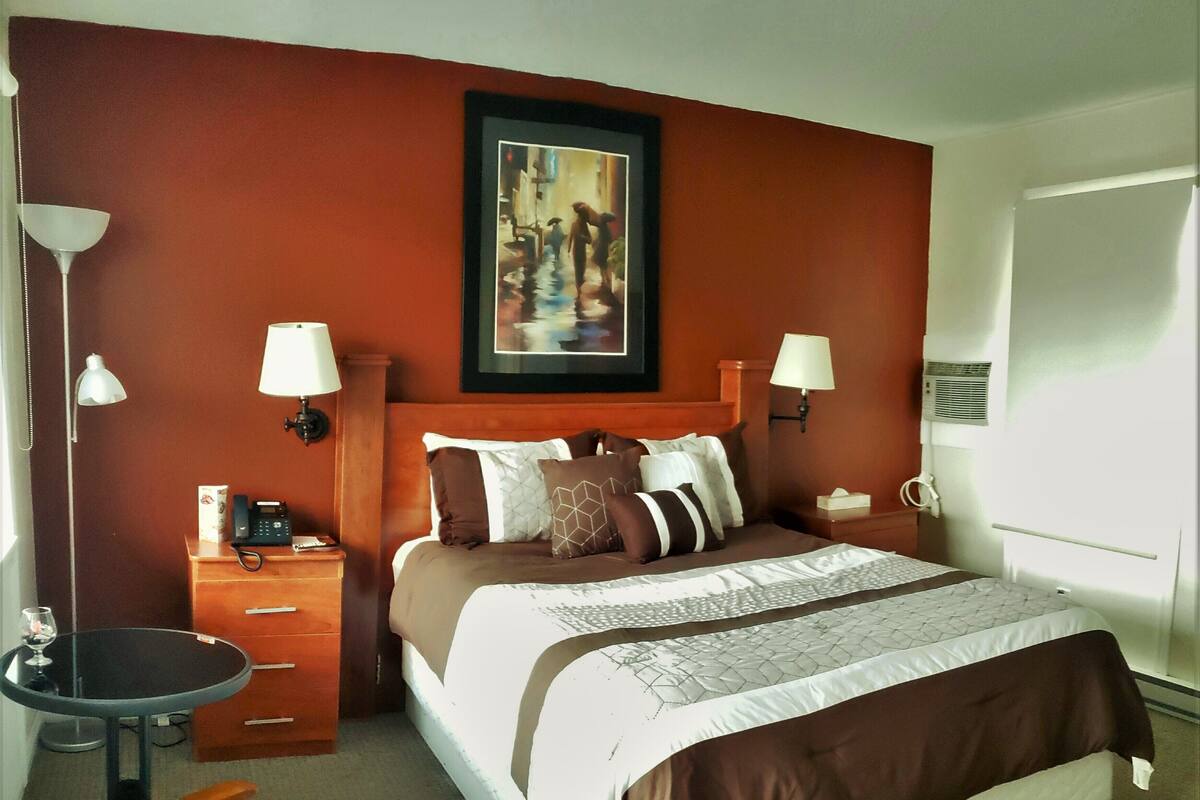 Una habitación de hotel con una cama, mesitas de noche, una silla, una lámpara y un cuadro en la pared.