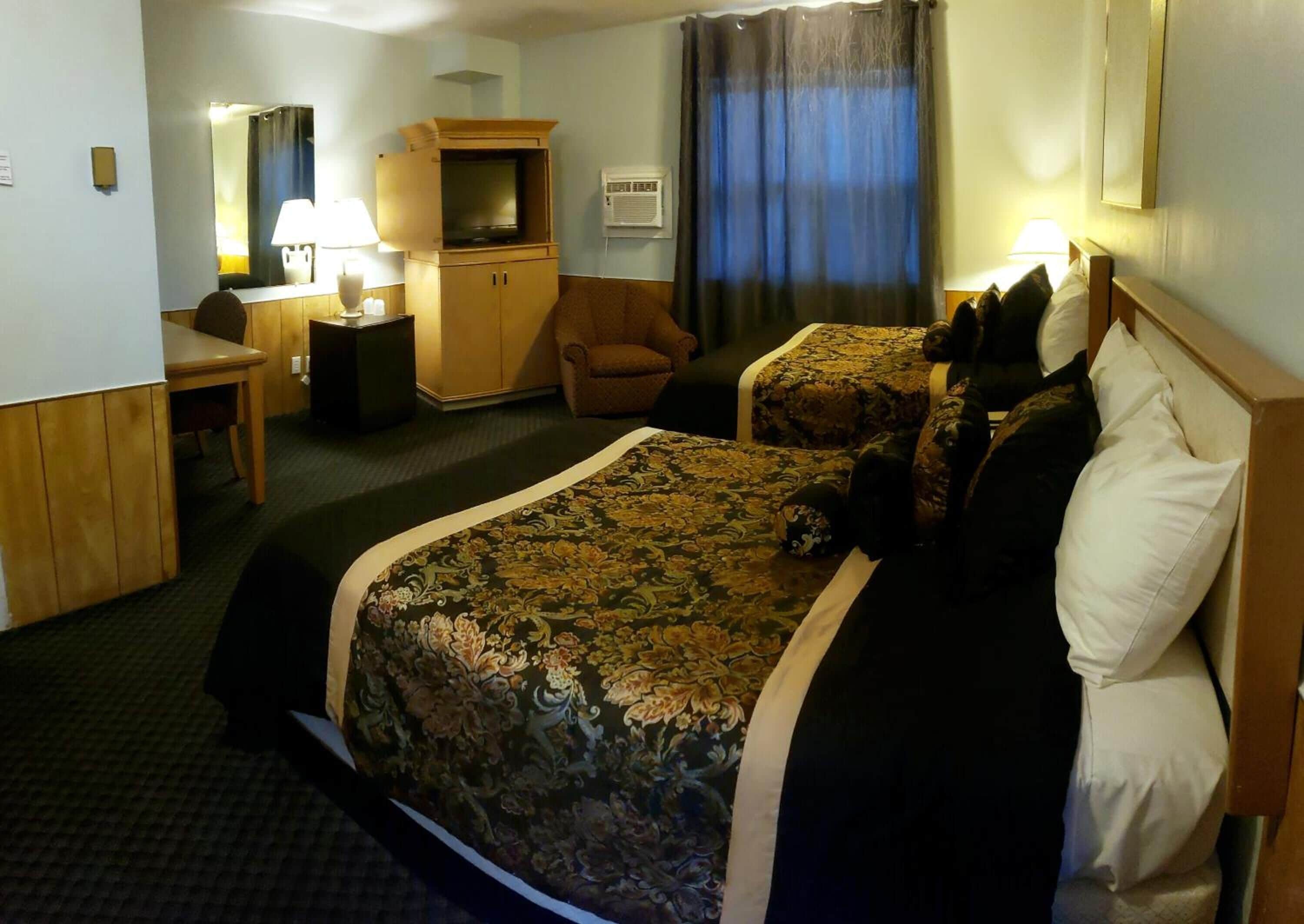 A hotel room with a large bed, two bedside tables, a desk, a chair, a television, and a wardrobe.