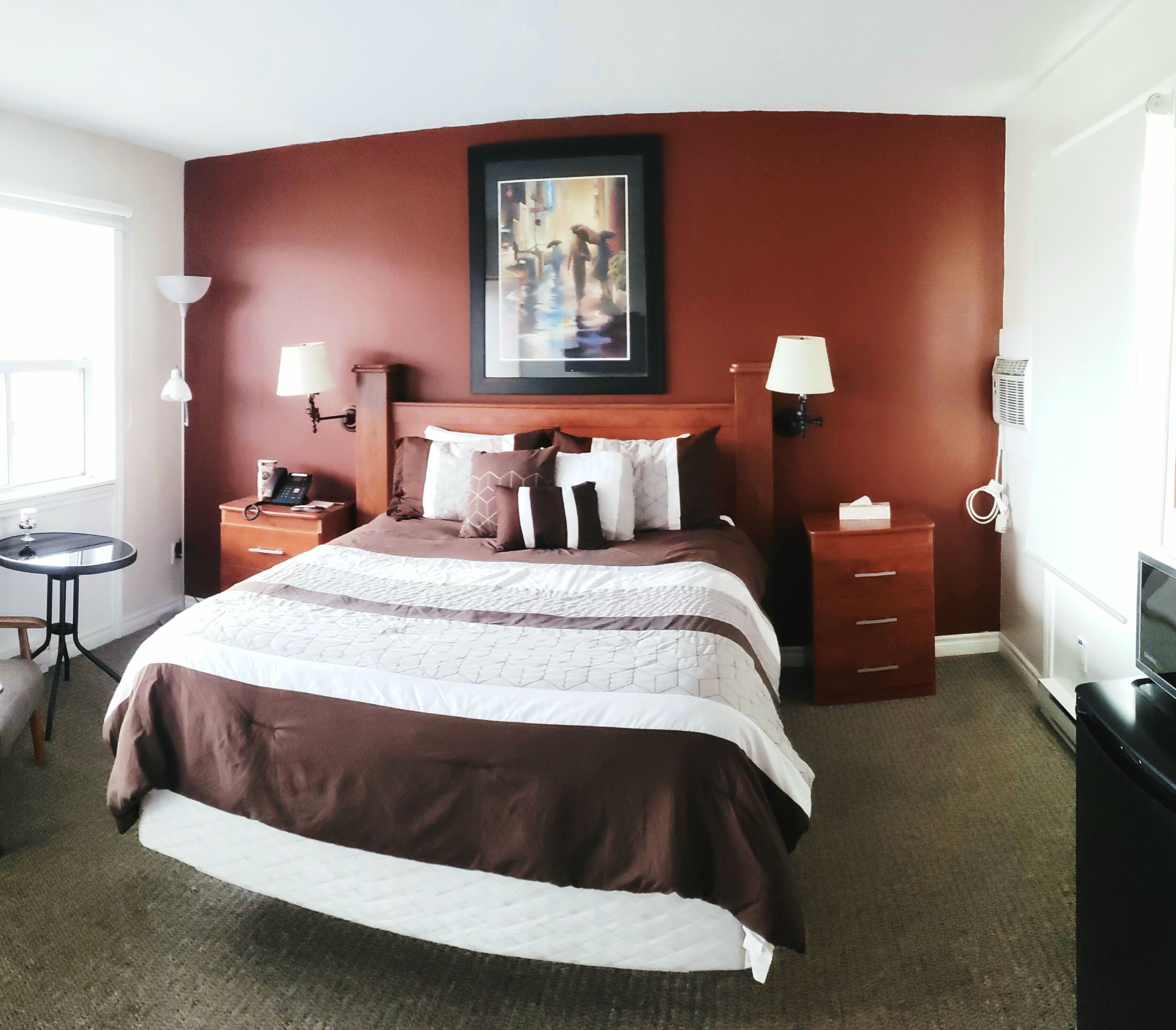 A hotel room with a large bed, two bedside tables, a desk, and a chair. There are two wall-mounted lamps and a painting above the bed.