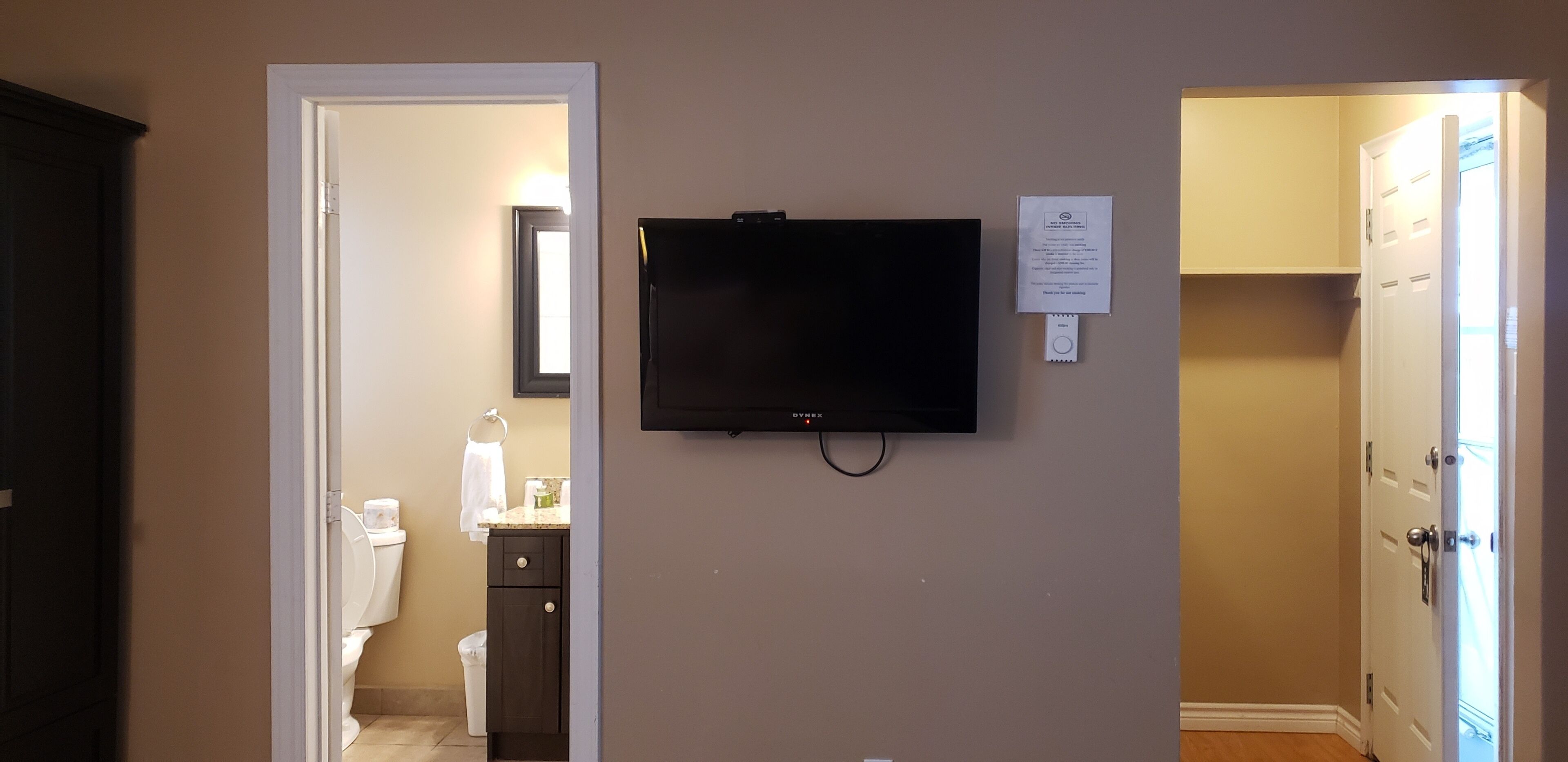 Una habitación con una televisión montada en la pared, una puerta que da al baño y un aviso en la pared.