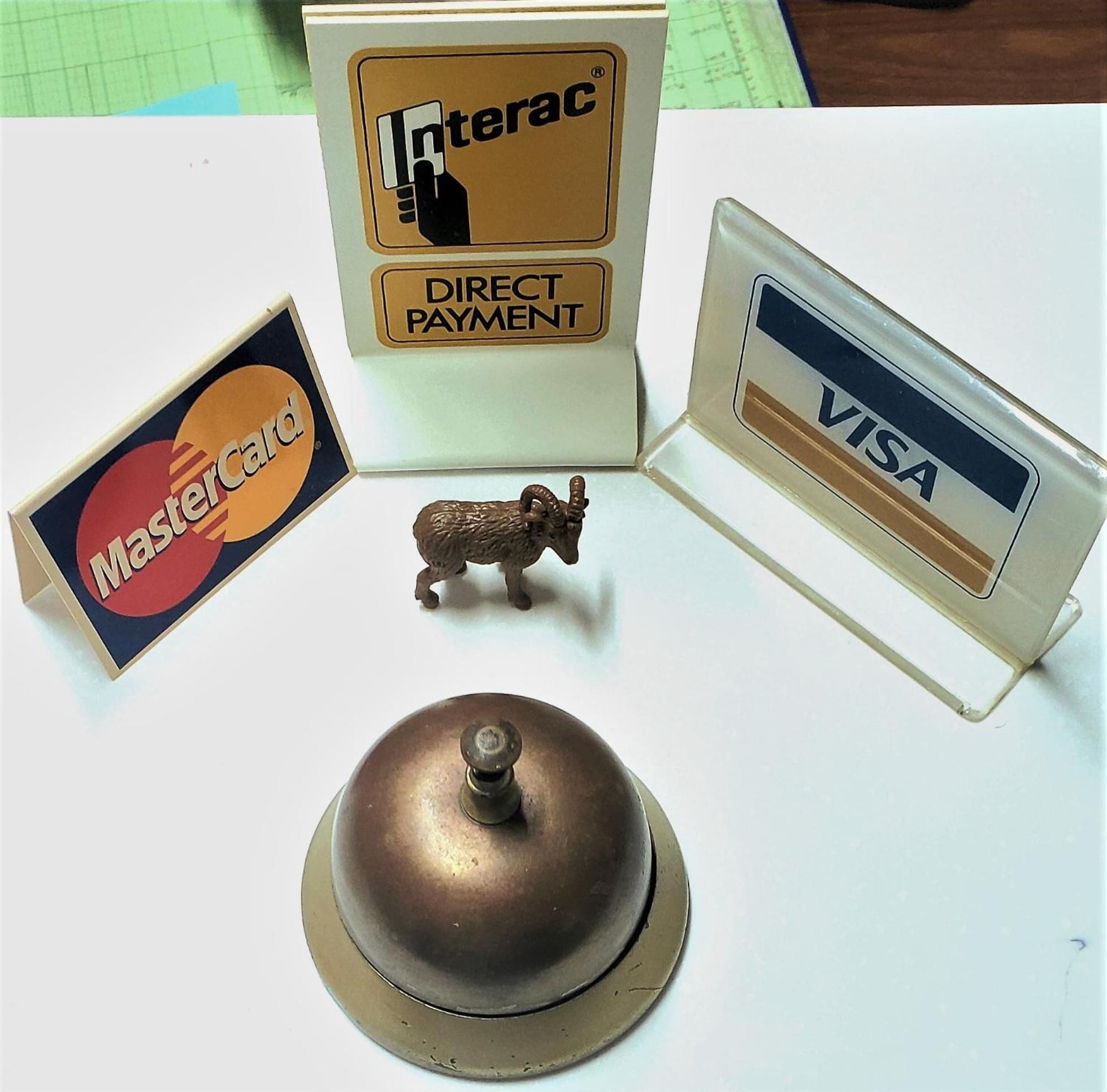 Een bureau met een koperen bel, een Mastercard logo, een Visa logo, en een Interac Direct Payment logo.