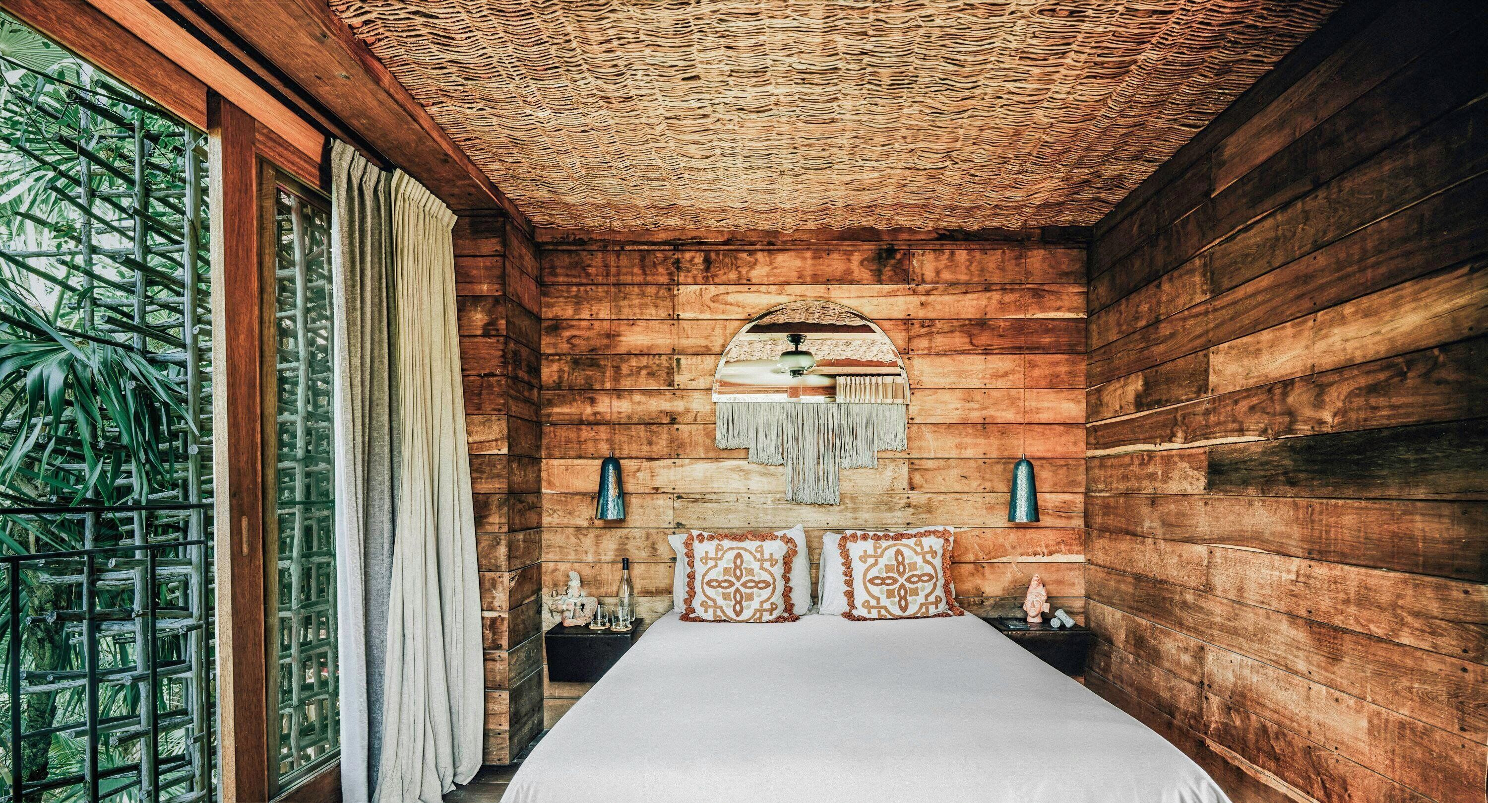 A wooden room with a bed, a window with curtains, a wall-mounted lamp, and a decorative wall piece.