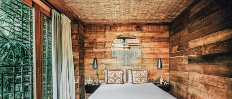 Una habitación de madera con una cama, una ventana con cortinas, una lámpara fijada a la pared y un adorno en la pared.