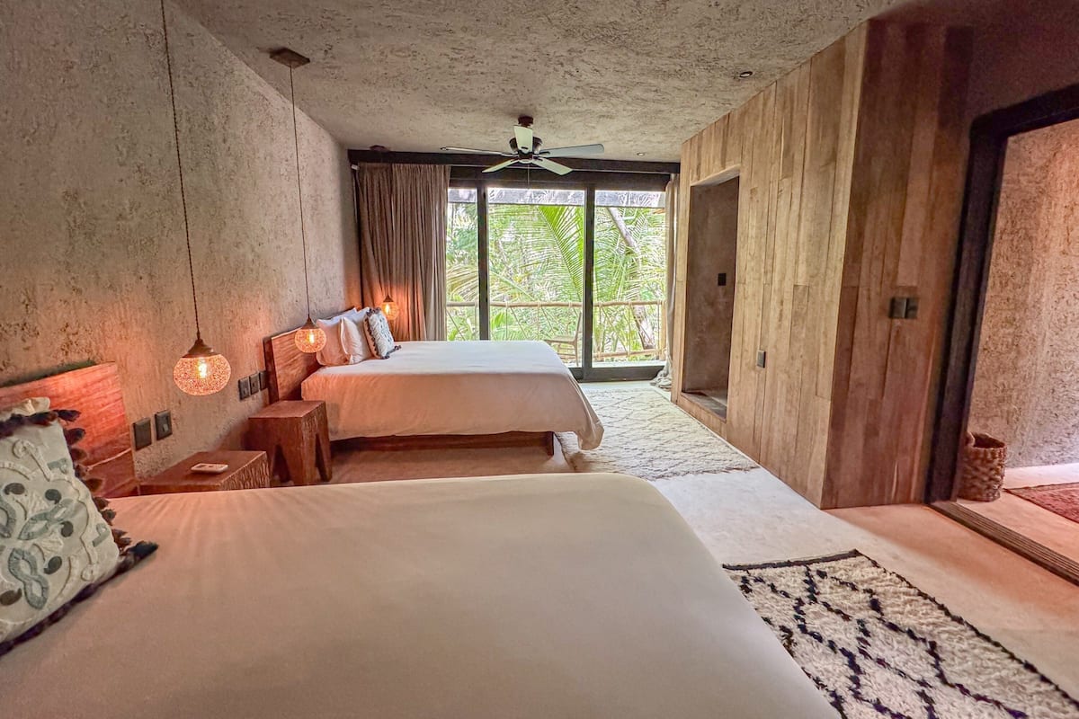 Un dormitorio con dos camas, un ventilador de techo y un ventanal con cortinas.