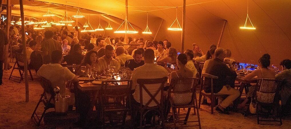 A tented dining area with tables and chairs, under a canopy with hanging lights.