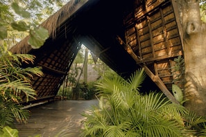A wooden bridge structure with a thatched roof, surrounded by lush greenery and trees.