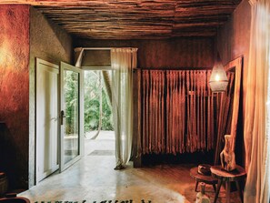 A room with a wooden ceiling, a door leading outside, a small table with a vase, and a hanging light fixture.