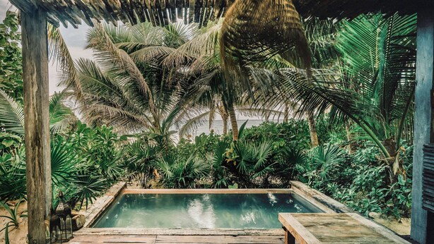 A pool area with a wooden deck, surrounded by lush tropical plants and a wooden pergola overhead. - Nômade Temple Tulum (Tulum)