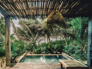 Een zwembadgedeelte met een houten terras, omgeven door weelderige tropische planten en een houten pergola.