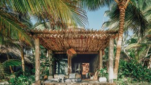 A covered outdoor seating area with steps leading up to it, surrounded by palm trees and greenery. - Nômade Temple Tulum (Tulum)