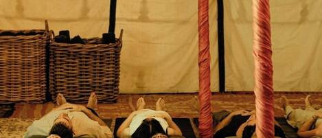 A group of people lying on mats in a tent-like structure with poles.