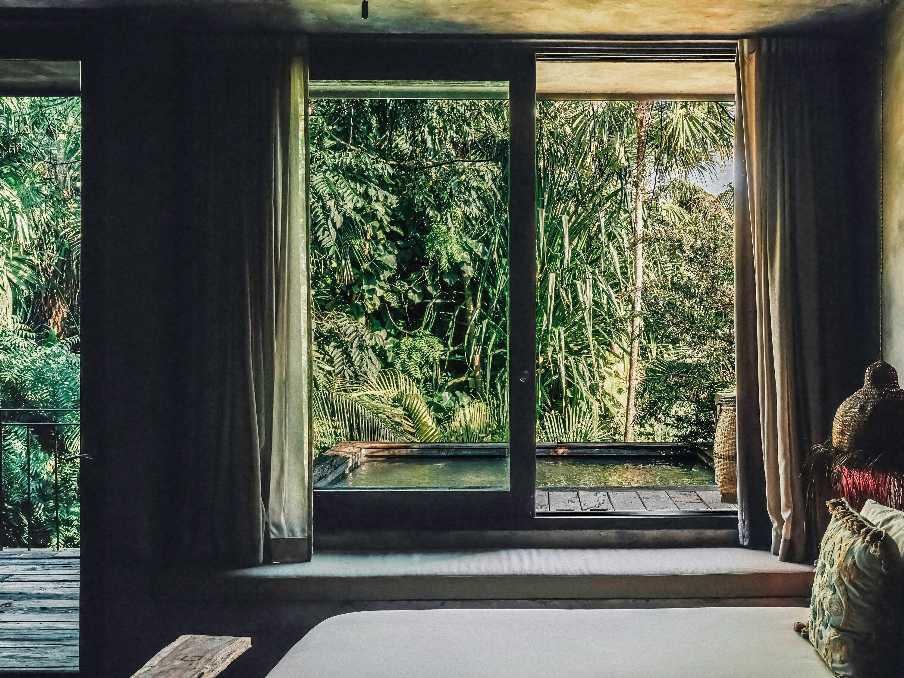 Una habitación con un ventanal grande, una cama y vistas a un jardín exuberante.