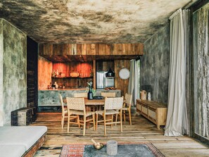 A rustic interior with a wooden dining table, chairs, and a kitchen area with wooden cabinets and a refrigerator.