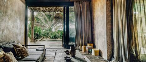 A room with a thatched roof, a sofa, a table, and a view of greenery outside.
