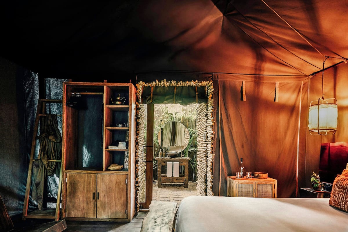 Una habitación con carpa, una cama, armarios de madera y una mesita con una planta.