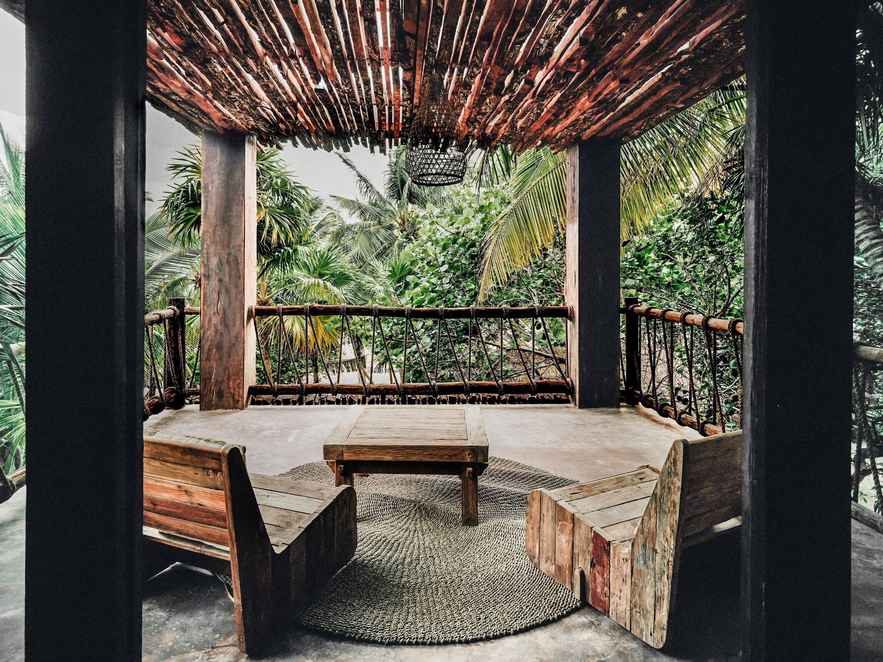 A wooden deck with a table and benches, surrounded by lush greenery.