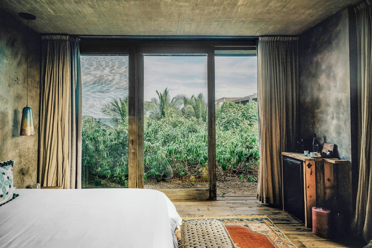 Un dormitorio con una cama grande, un escritorio de madera y vistas a un jardín tropical a través de puertas de vidrio.