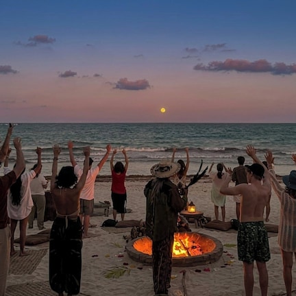 A group of people at a beach with a fire pit in the foreground.