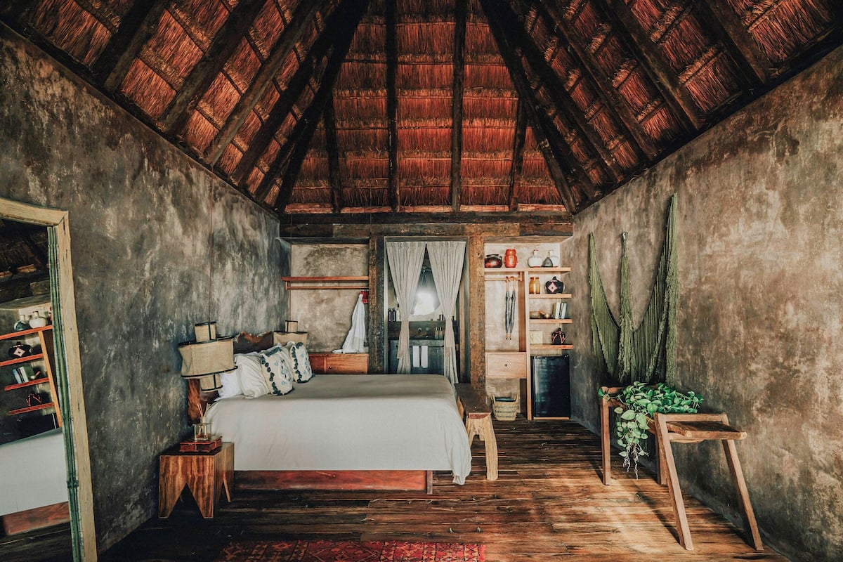 Un dormitorio rústico con techo de madera, una cama, una mesita de noche, un aparador y una pequeña mesa con una planta.