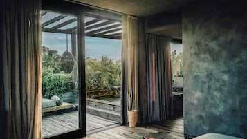 A room with a large sliding glass door leading to a wooden deck, a bed, and a woven rug.