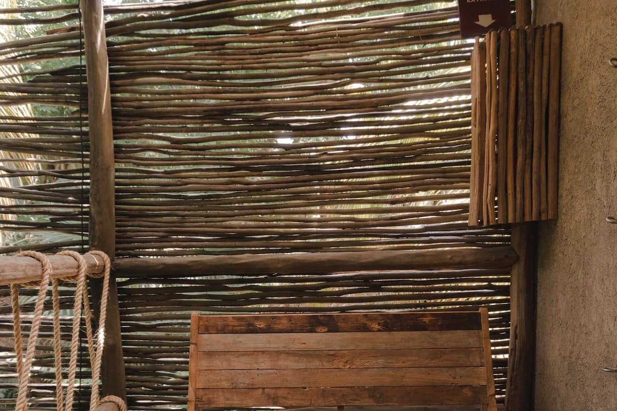Un banco de madera y un taburete en una habitación rústica con pared de bambú y puerta de madera.